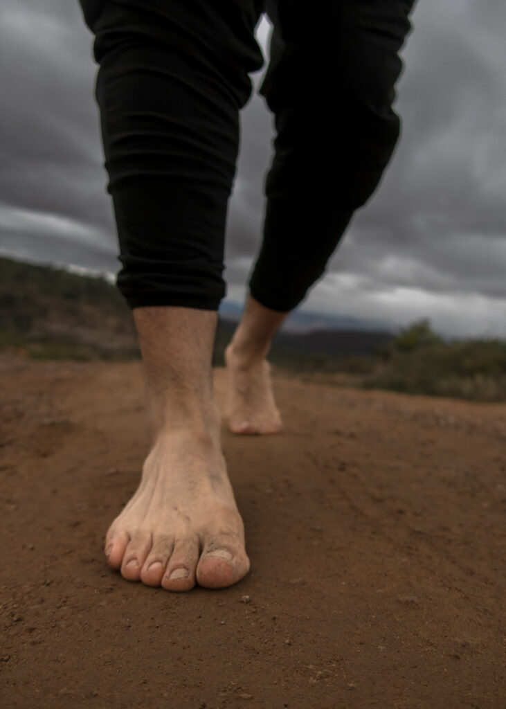 man walking barefoot on dirt road and rocks