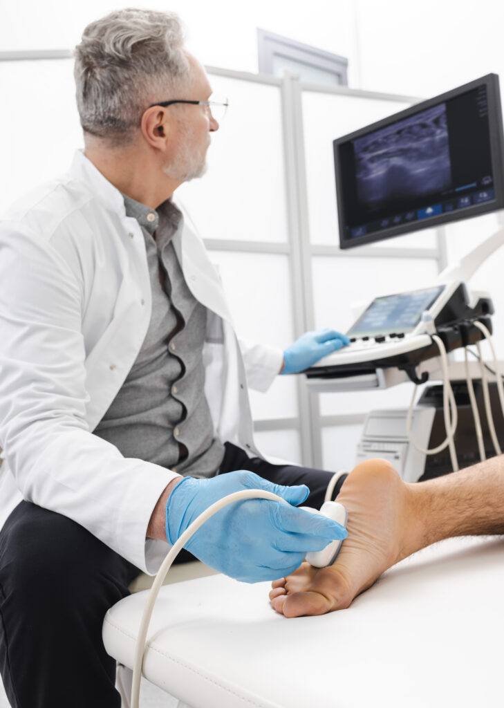 attentive doctor sonographer looking at ultrasound screen while scanning sole of injured foot of patient in diagnostic room of clinic